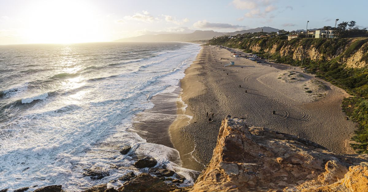 Stunning aerial view of the coastline at sunset, featuring waves crashing on the sandy beach in Malibu.